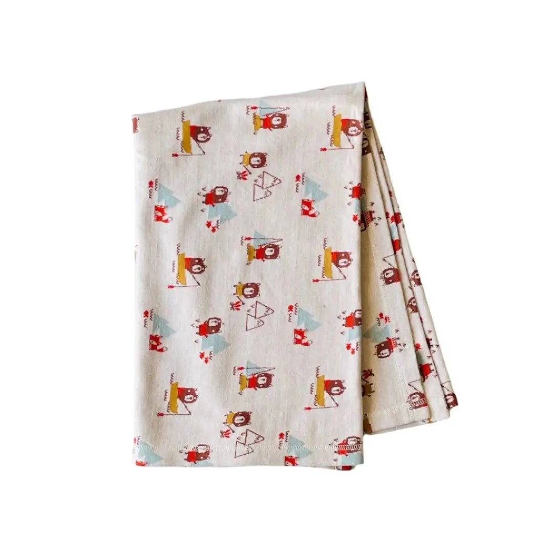 This image shows a folded baby blanket made from organic cotton, featuring a whimsical pattern of bears, foxes and trees.
