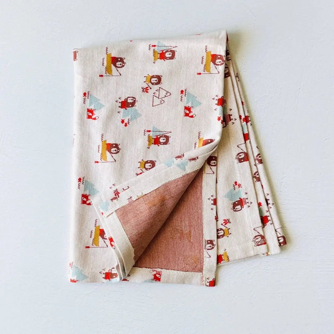 This image features a folded organic cotton baby blanket with a playful camping-themed print.