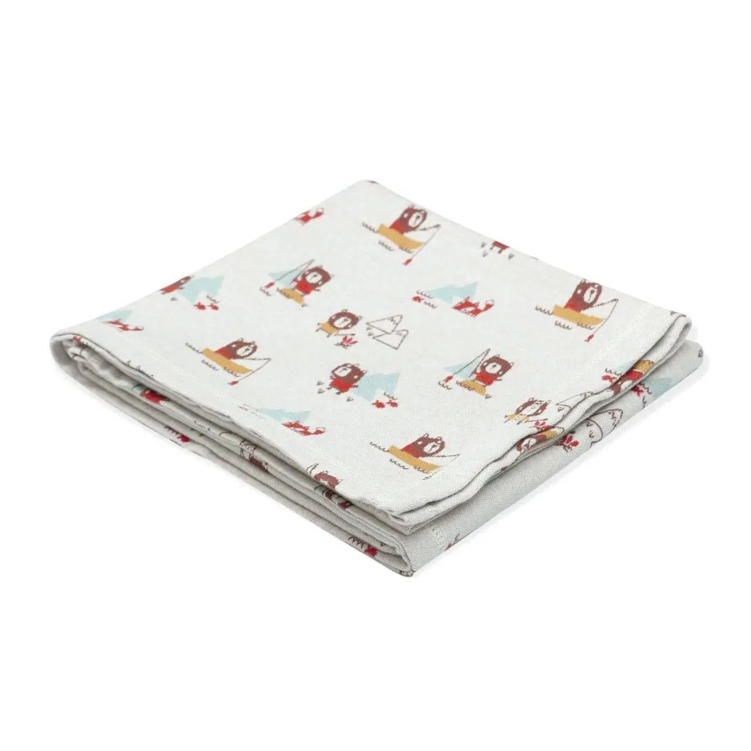 This image displays a neatly folded baby blanket made from organic cotton with a camping-themed print.