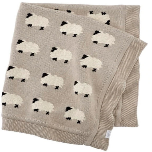 Taupe-colored knit baby blanket folded to show a pattern of white sheep with black faces and legs, bordered with a ribbed texture along the edges.