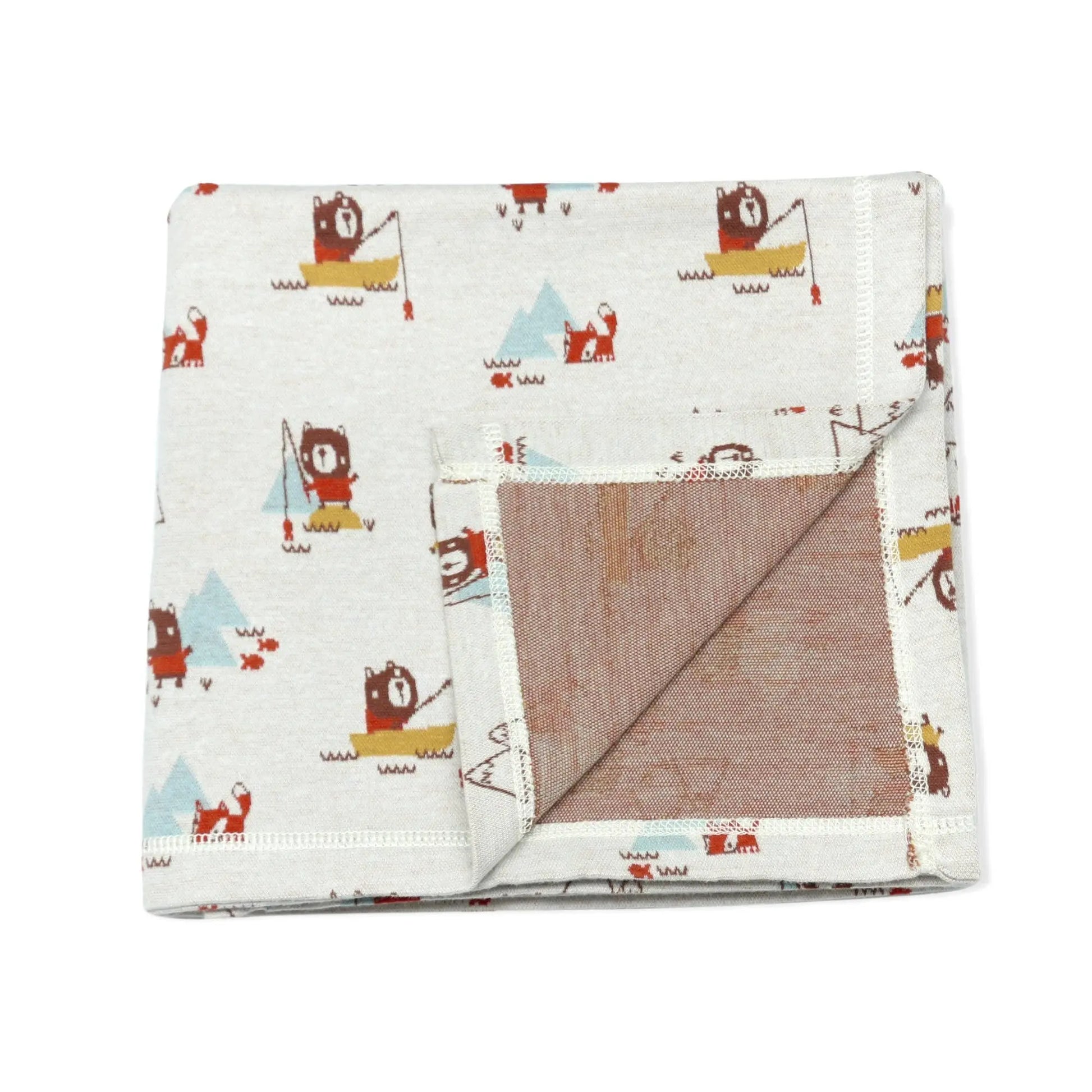 This image showcases a folded organic cotton baby blanket with a fun, camping-themed design featuring bears, foxes, mountains, and fishing scenes. One corner of the blanket is flipped over, revealing a solid light brown reverse side. The playful illustrations make this blanket perfect for nature-loving families or those who enjoy outdoor-inspired decor for their little one's space.