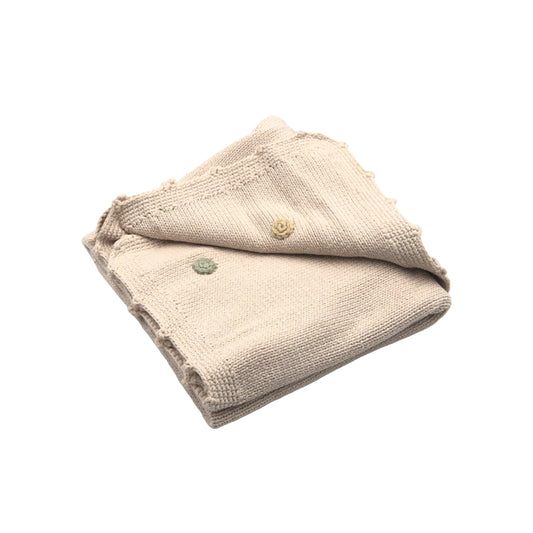 Neatly folded cream colored knitted baby blanket with decorative colored buttons in green and yellow, showcasing a subtle textured weave.