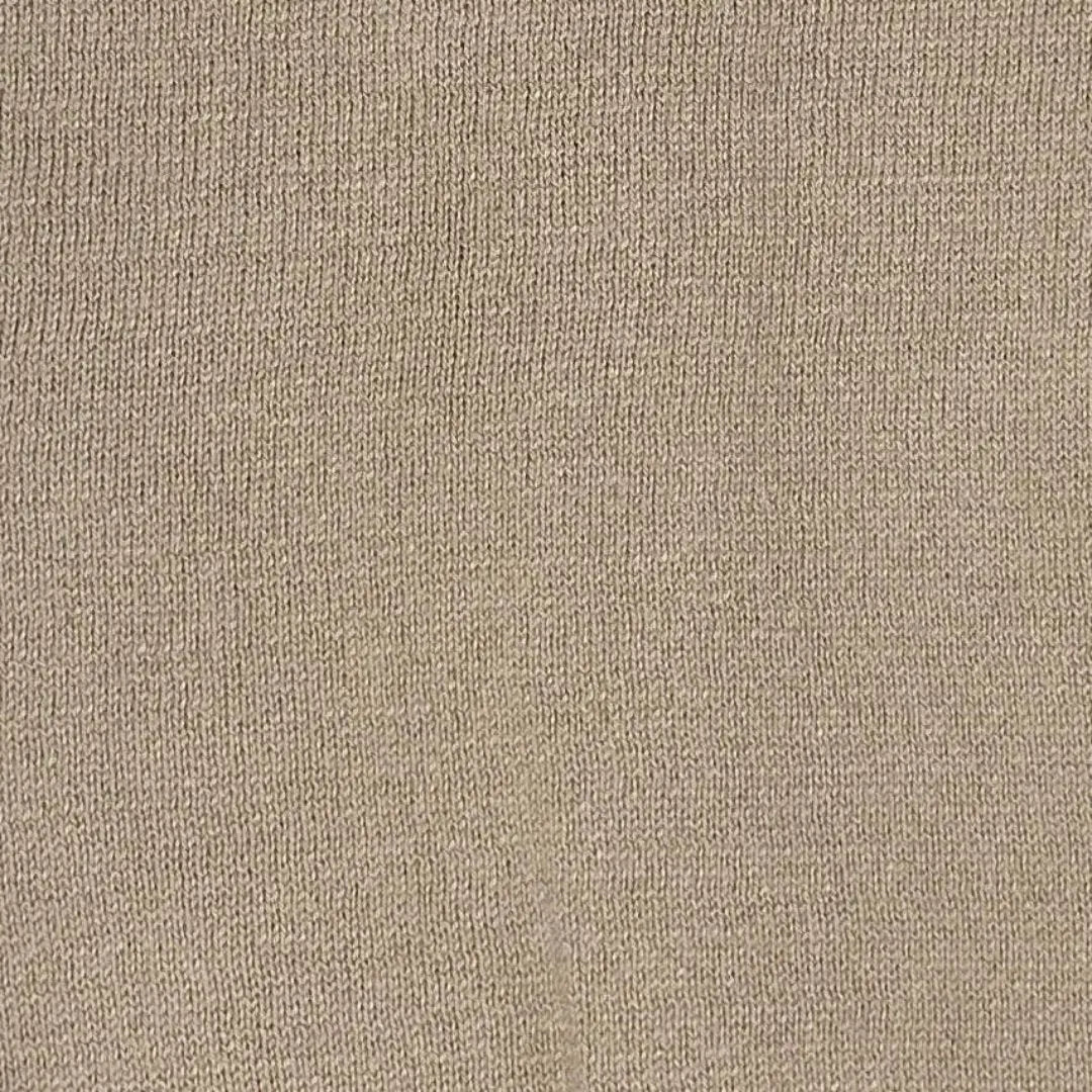 This image is a close-up of a beige knit fabric, showcasing its texture and weave. The material appears soft and slightly stretchy, with a fine, even pattern, likely from a sweater or poncho. The neutral tone suggests versatility for casual or cozy outfits.