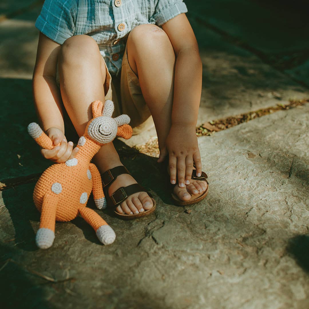 Child holding a crochet deer toy on a stone surface