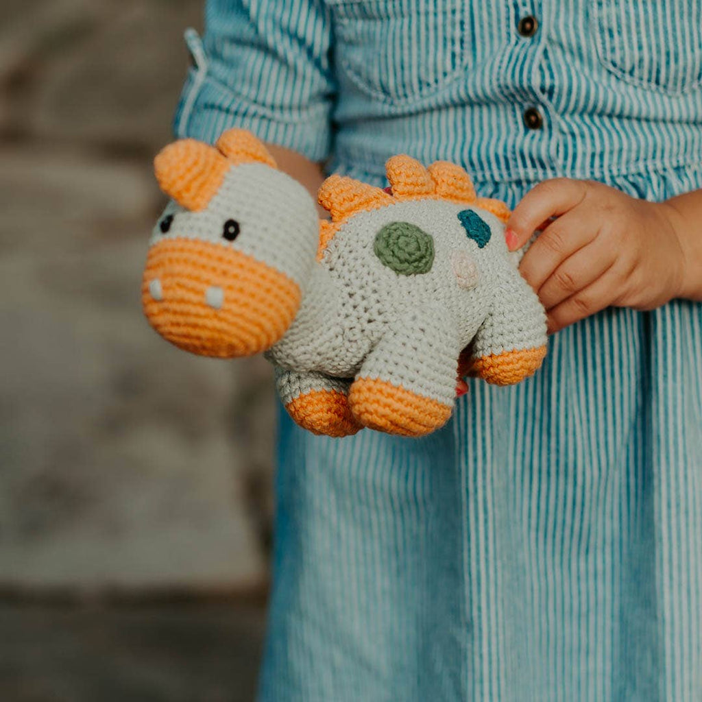 Child holding a crocheted dinosaur toy with a blurred background
