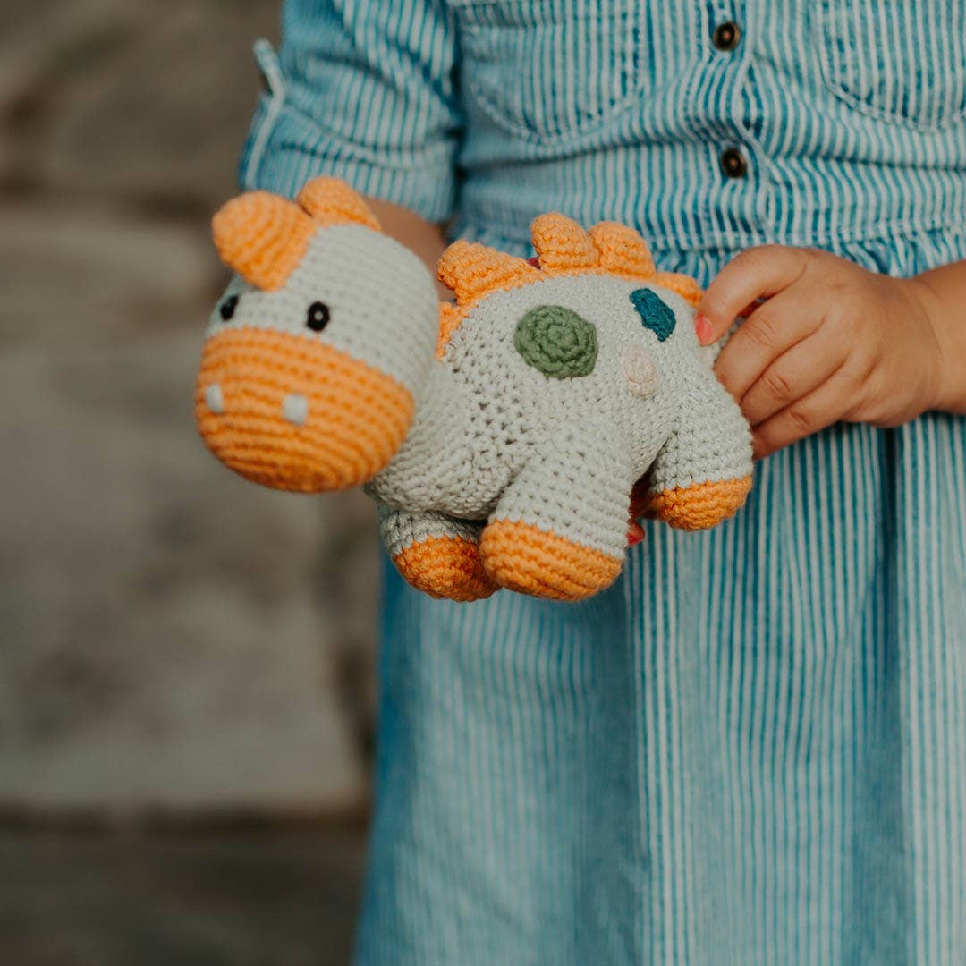 Child holding a crocheted dinosaur toy with a blurred background