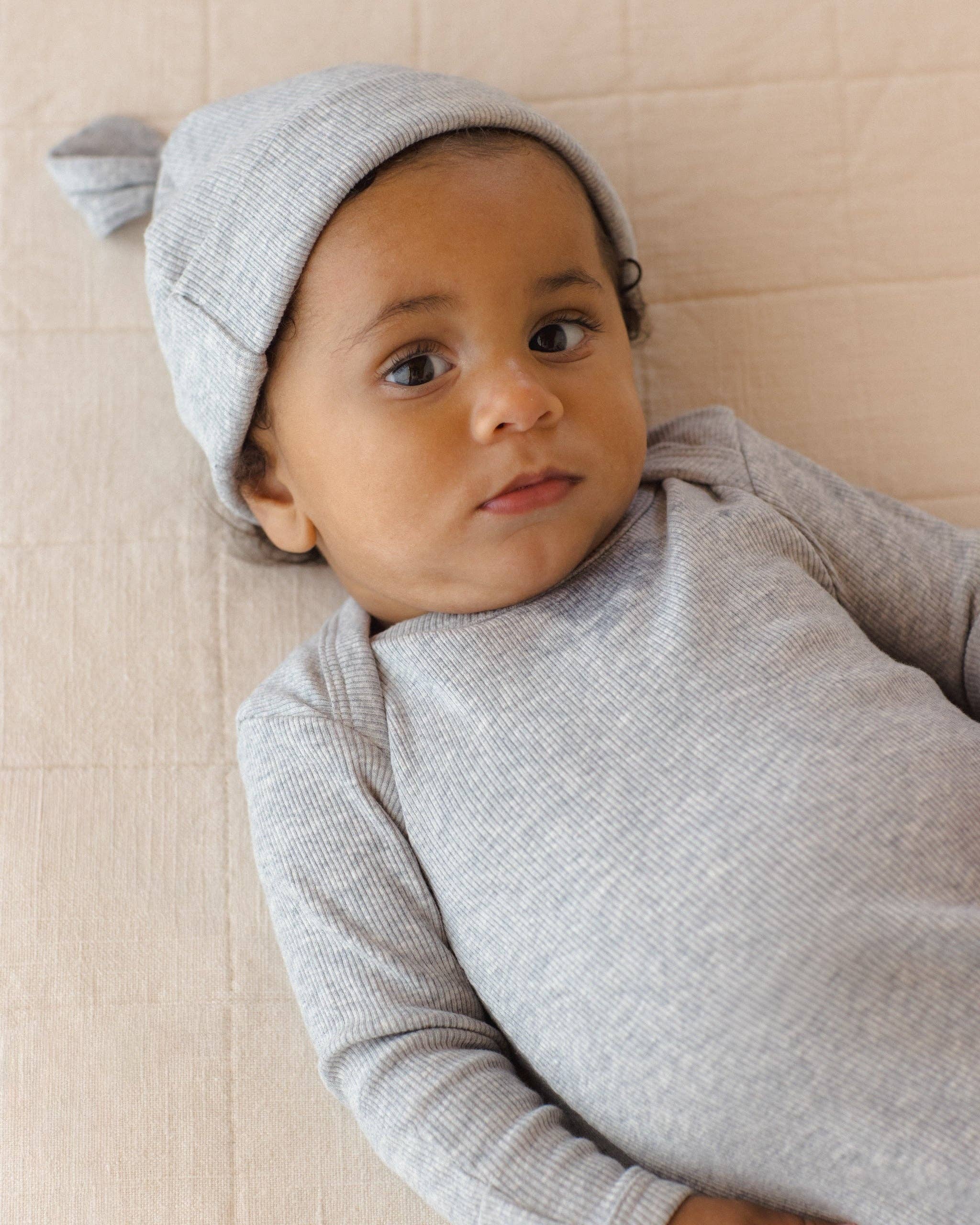 Baby wearing a gray knit outfit and hat on a beige background