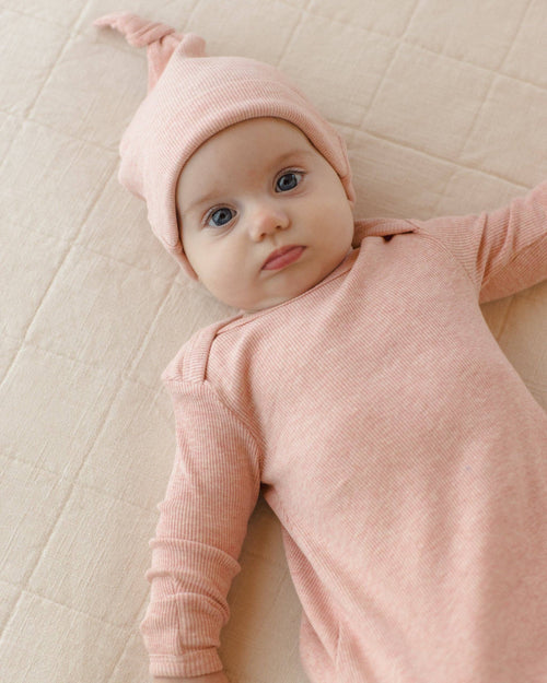 Baby wearing a pink outfit and hat lying on a beige surface