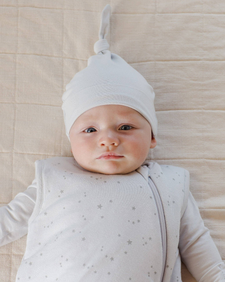 Baby wearing a white hat and light gray onesie with star pattern on a beige textured background