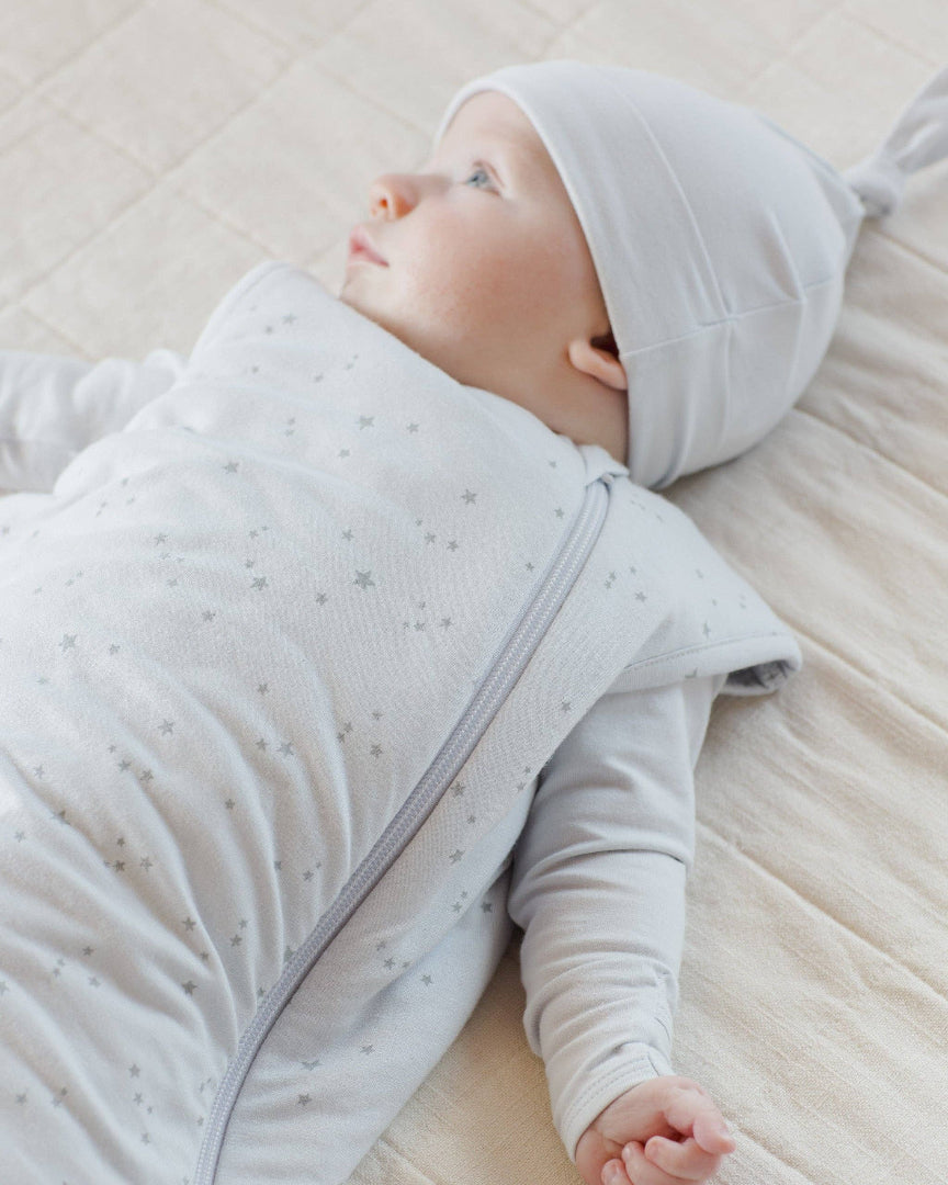 Baby wrapped in a light gray swaddle with star pattern on a soft beige surface