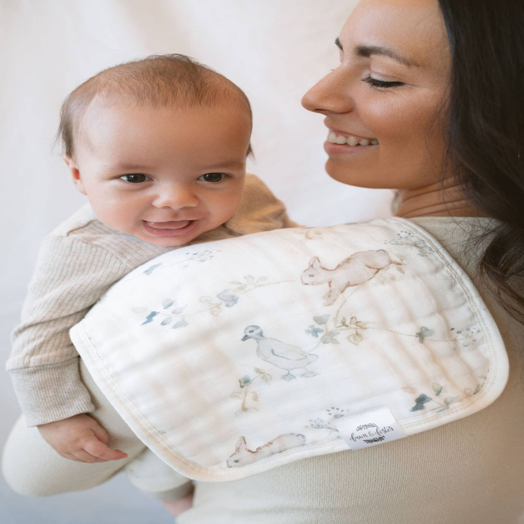 Woman holding a baby with a burp cloth featuring animal prints.