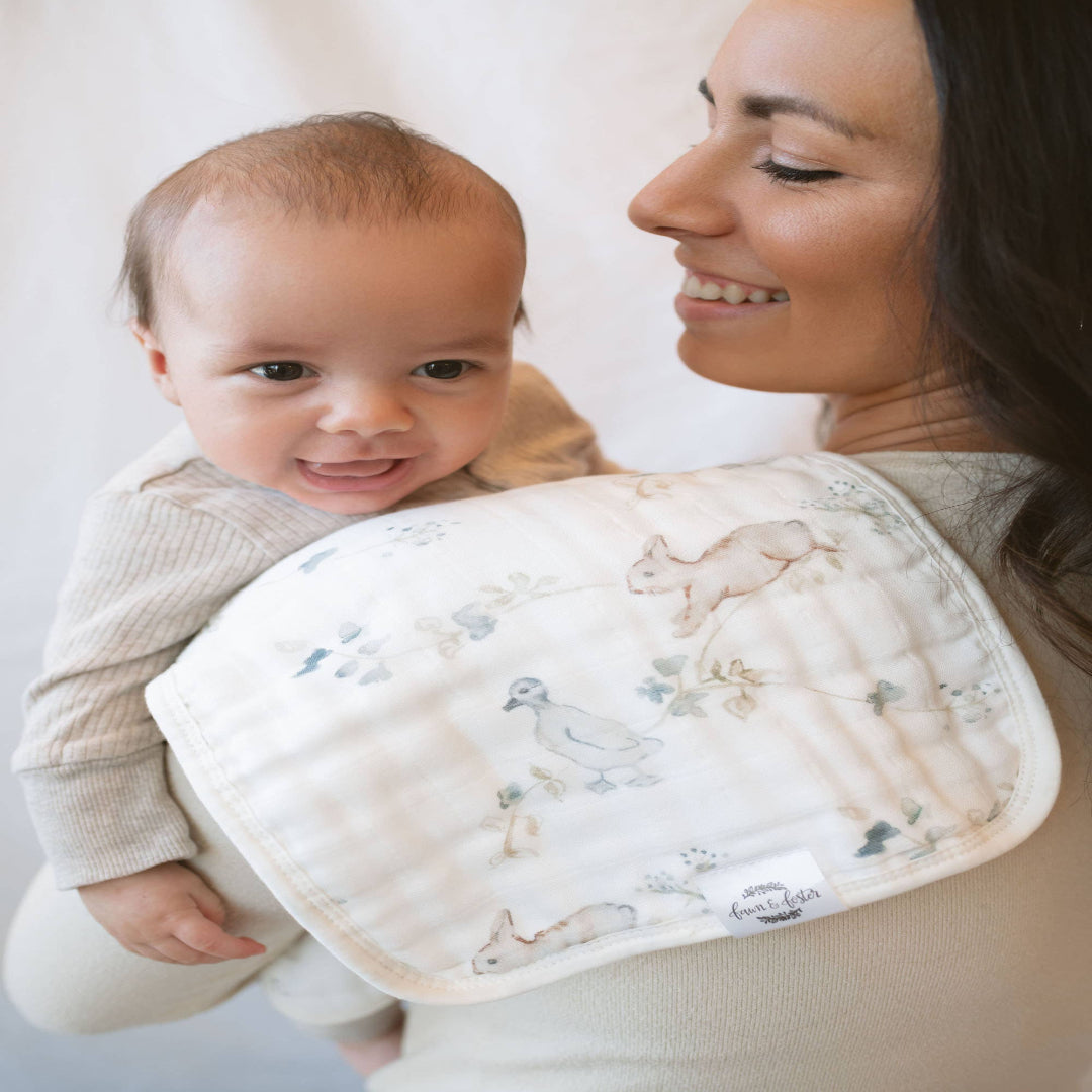 Woman holding a baby with a burp cloth featuring animal prints.